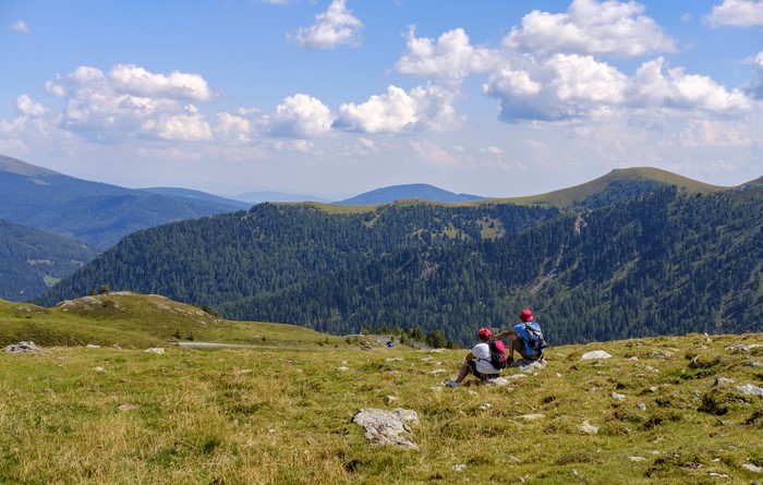 Two hikers resting on a mountain with forested slopes