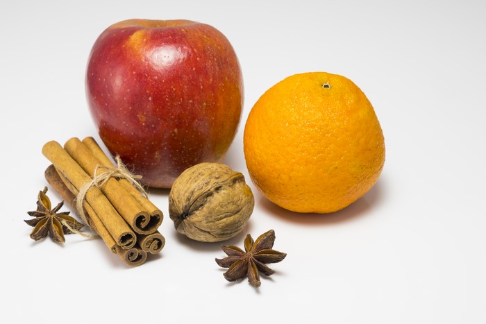 Apple, orange, cinnamon sticks, walnut, and star anise on white background