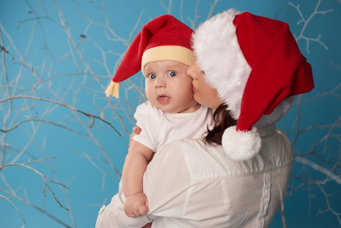Mother kissing baby wearing Santa hats