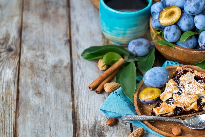 Plum pie with plums and coffee on wood planks