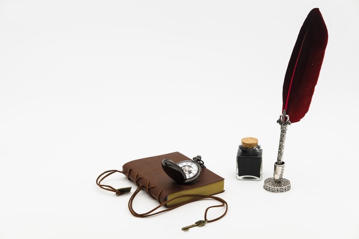 Feather quill, inkwell, pocket watch, and key on a book