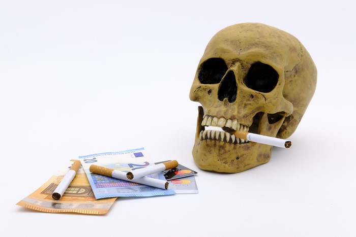 Skull with cigarettes and Euro banknotes on white background