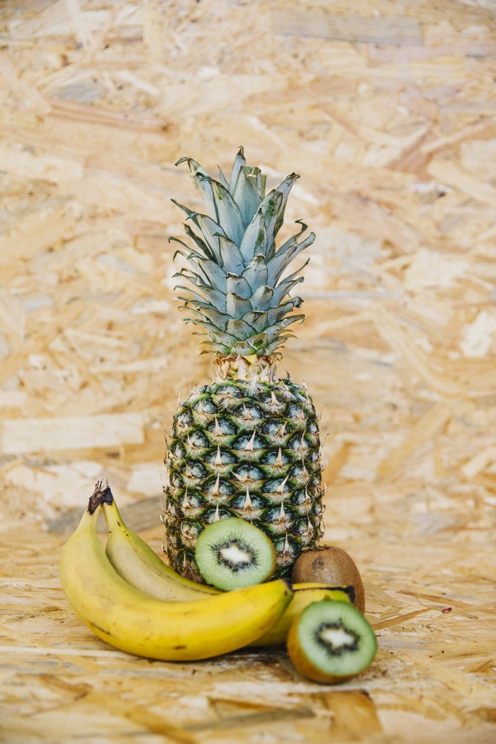Pineapple, bananas, and kiwi fruit on a wooden background