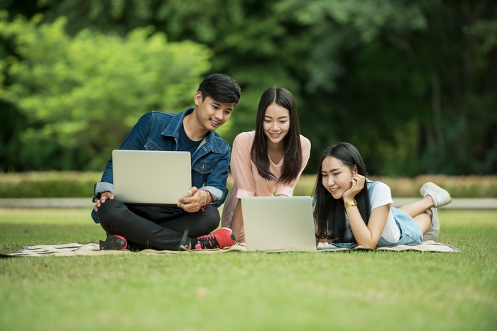 Three students with laptops on grass