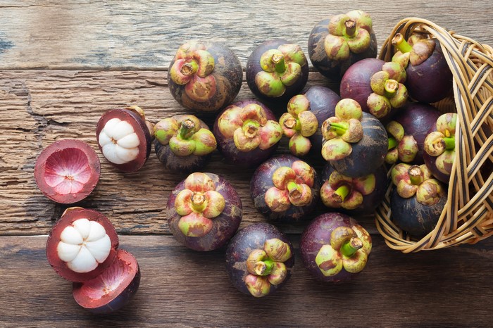 Mangosteens in a wicker basket on wood planks