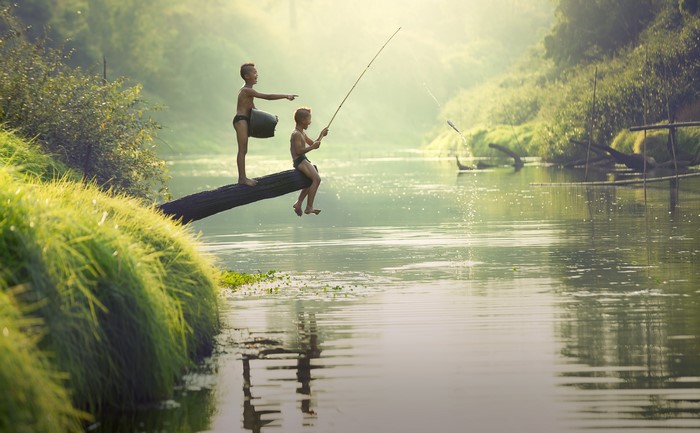 Two Asian boys fishing on a log