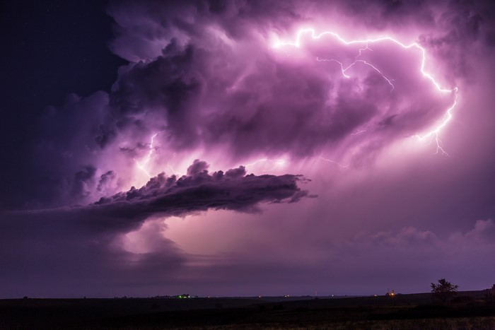 Lightning strikes through purple storm clouds over a dark landscape