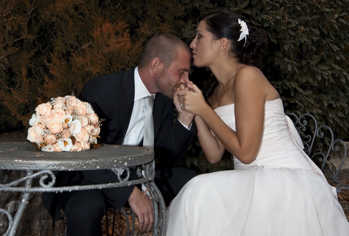 Bride kissing groom's hand with bouquet on table