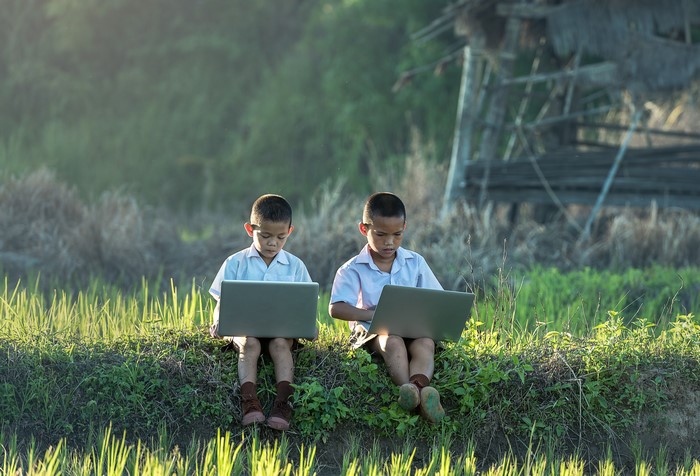 Two Asian boys in school uniforms using laptops outdoors
