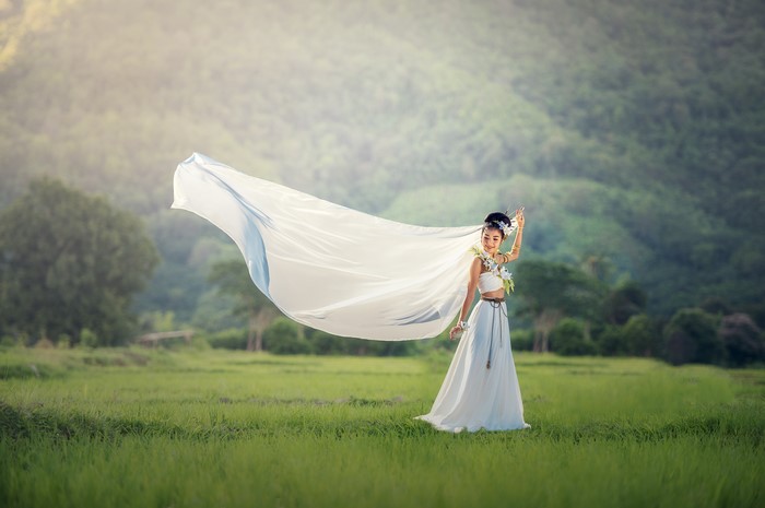 Asian woman in white dress with flowing fabric in a field