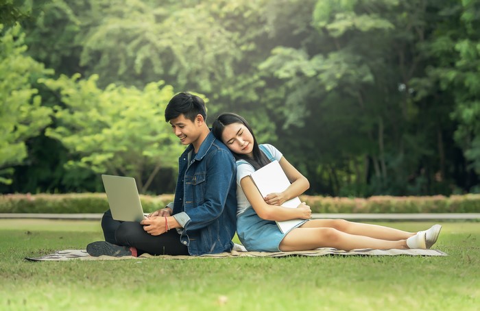 Asian couple with laptops on grass