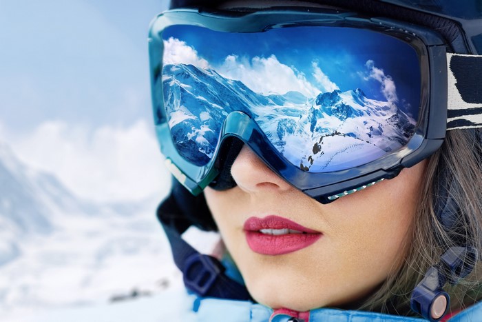 Woman wearing ski goggles reflecting mountains