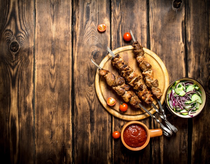 Shashlik with salad and ketchup on a wooden board