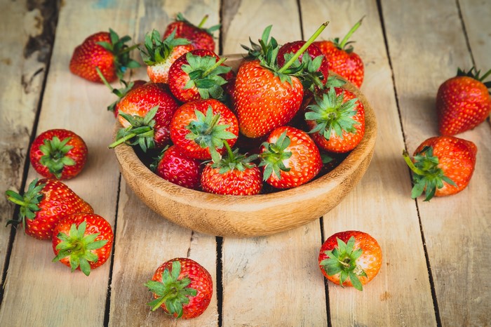 Strawberries in a wooden bowl on wood planks