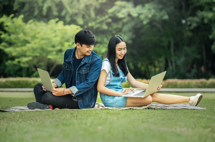 Asian couple using laptops in a park
