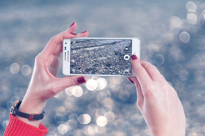 Hands holding Samsung smartphone taking picture of water and pebbles