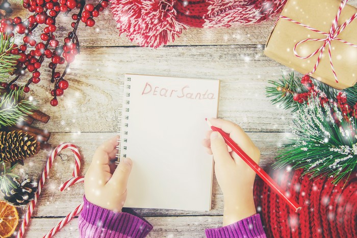 Child writing 'Dear Santa' on notepad with Christmas decorations