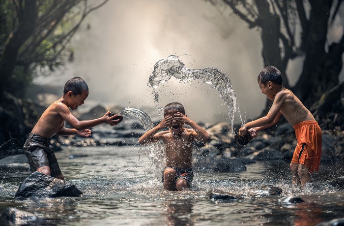 Three boys splashing water in a stream