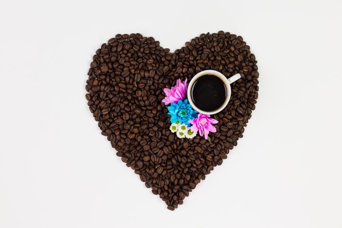 Heart shape made of coffee beans with a cup and flowers