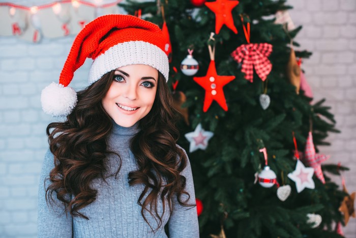 Woman in Santa hat and sweater near Christmas tree