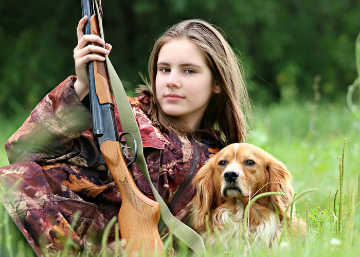 Girl with shotgun and dog in grass