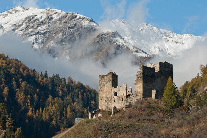 Ruins of a castle on a hill with snowy mountains and fog
