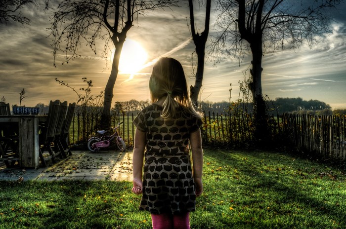 Girl in backyard at sunset with fence and trees