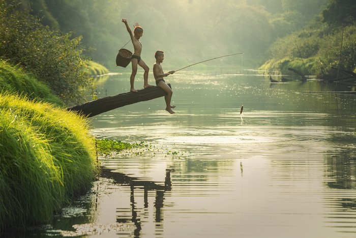 Two Asian boys fishing from a log in a river