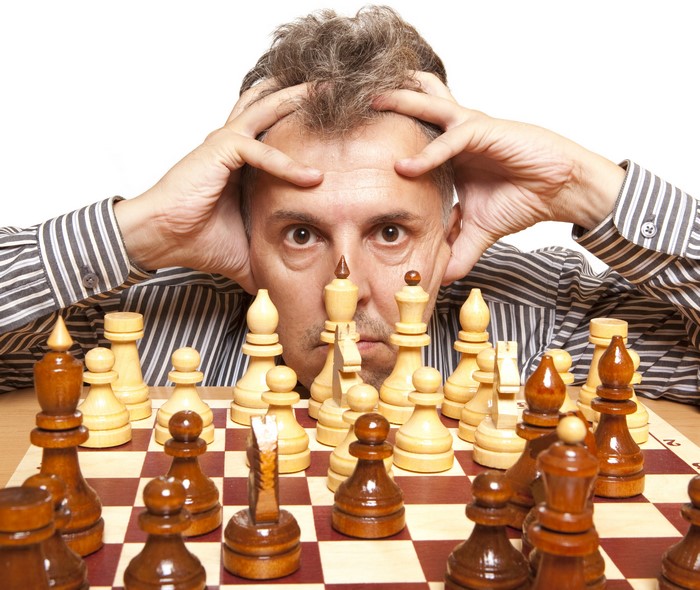 Man playing chess with hands on head