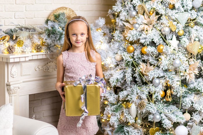 Girl holding a gift in front of a Christmas tree