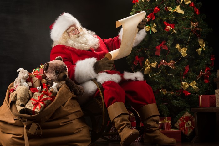 Santa Claus reading a list by a Christmas tree
