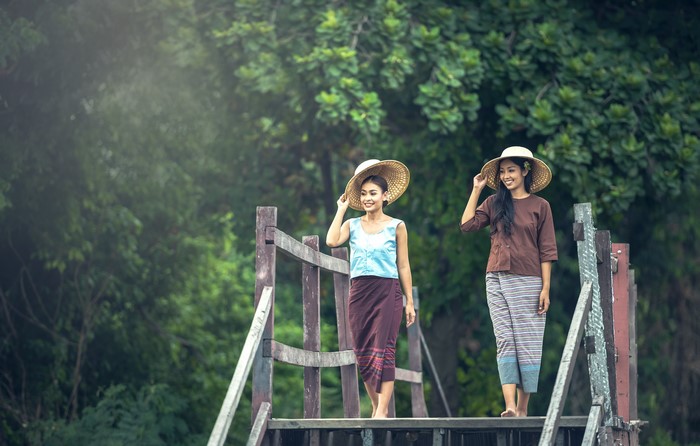 Two Asian women in traditional clothing and hats on a wooden bridge