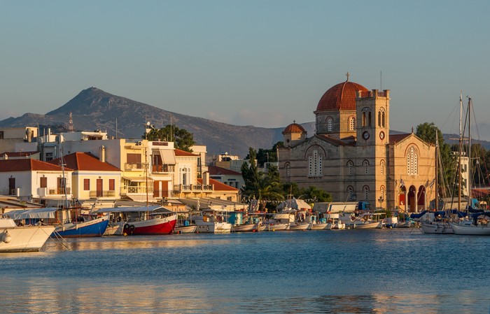 Boats docked in a Greek harbor with a church and mountains