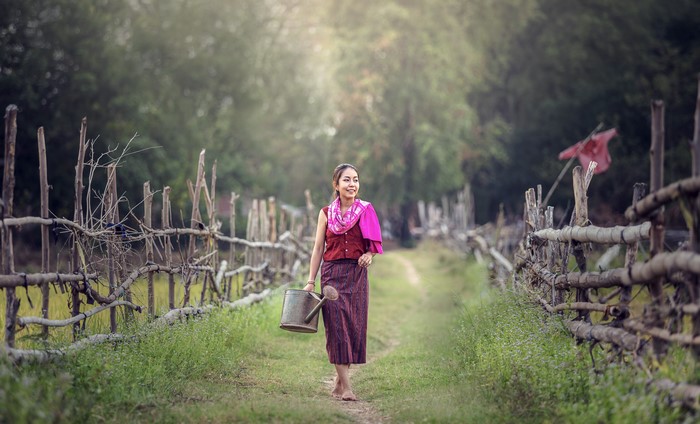 Asian woman with watering can on a rural path