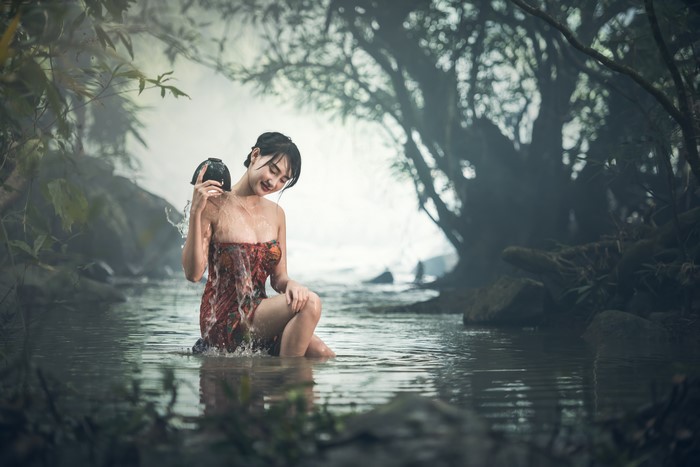 Asian woman bathing in a stream with a pot
