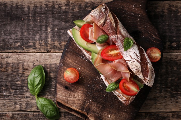 Sandwich with ham, avocado, and tomatoes on a cutting board