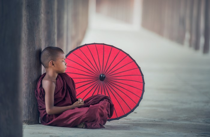 Young monk sitting with red umbrella