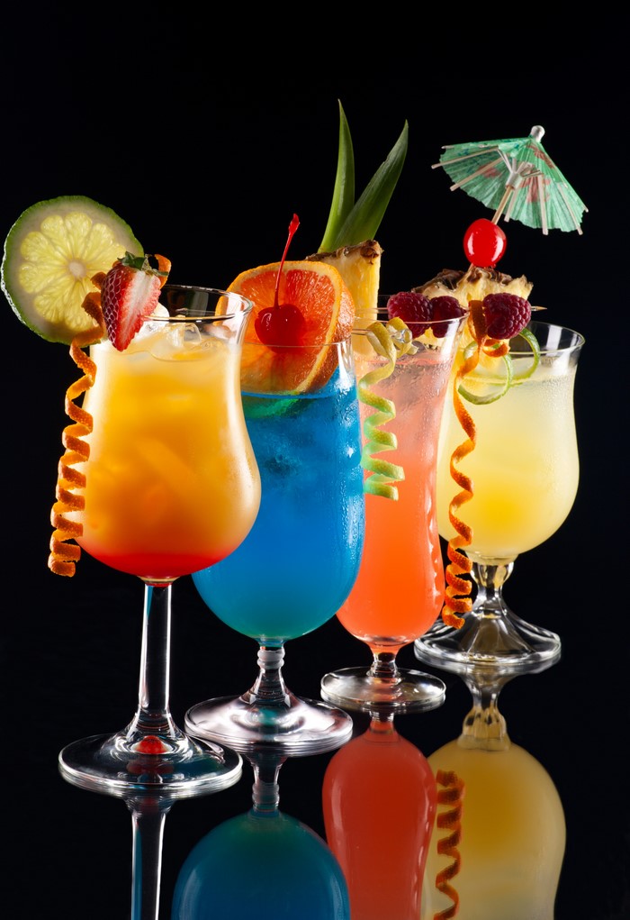 Four colorful cocktails with fruit garnishes on a black background