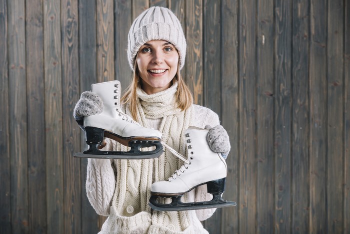 Blonde girl in winter hat holding ice skates