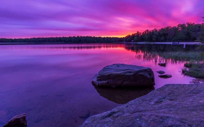 Purple sunset over a calm lake with rocks