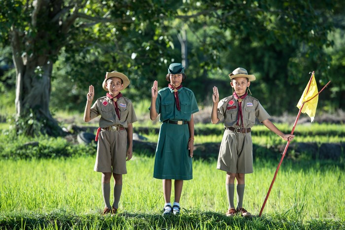 Three scouts in uniform raising their hands