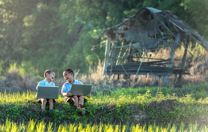 Two Asian boys laughing with laptops in a rural setting