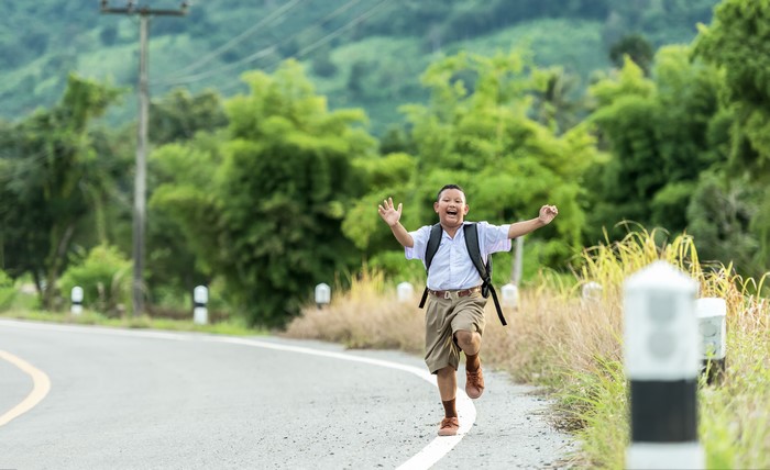 Asian boy in school uniform running on road