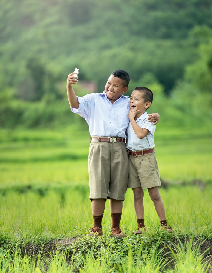 Two Asian schoolboys taking a selfie in a field