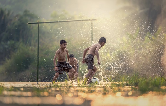 Three Asian boys playing football in water splashes