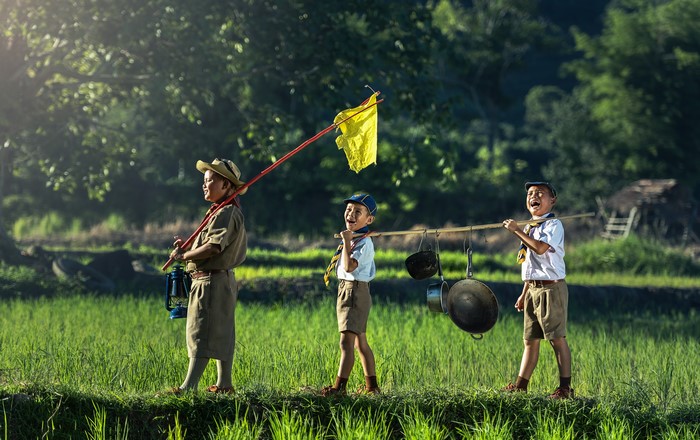 Three boys in scout uniforms walking through a field