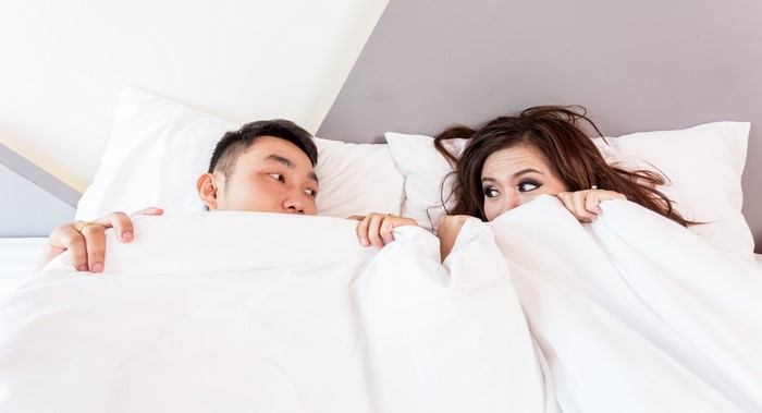 Couple peeking from under the covers in bed