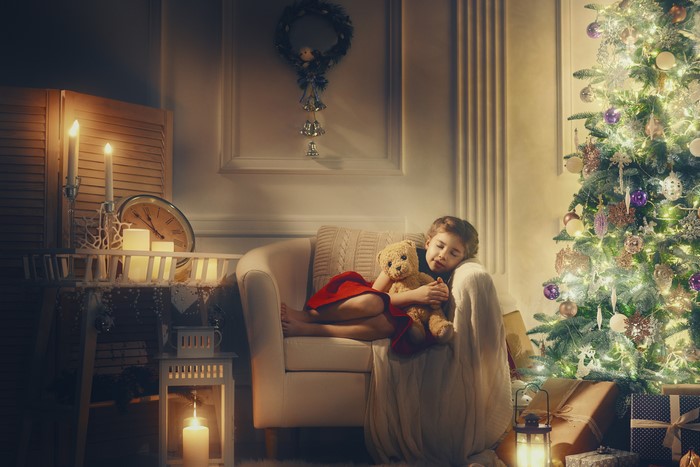 Girl sleeping with teddy bear by Christmas tree