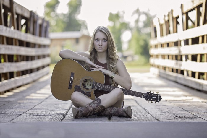 Woman sitting on wooden bridge with guitar