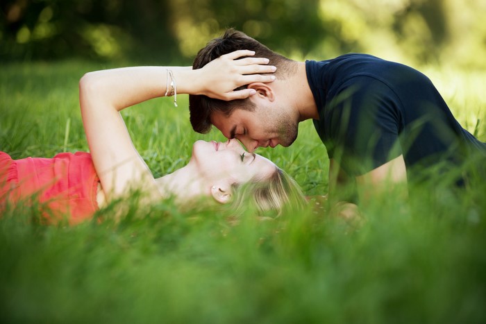 Couple lying in grass, about to kiss